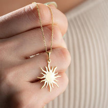 Gold sun-shaped pendant necklace on a hand against a neutral background