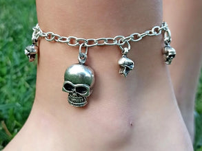 Silver anklet with skull charms on a person's ankle against a grassy background