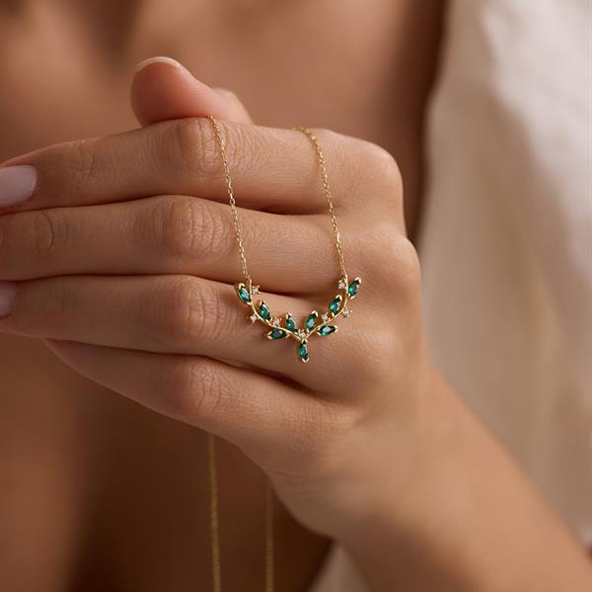 Gold necklace with green gemstones held in a hand against a neutral background