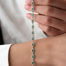 Hand holding a green gemstone bracelet against a neutral background