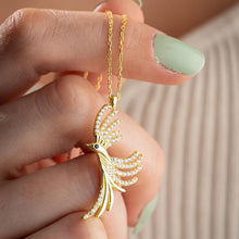Gold bird-shaped pendant necklace held by a hand with light green nail polish.