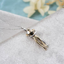 Silver and gold necklace pendant on a light gray surface with a blurred floral background