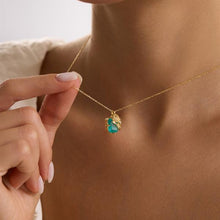 Gold necklace with a green gemstone pendant being adjusted by a hand.