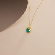Gold necklace with a green teardrop pendant on a beige background