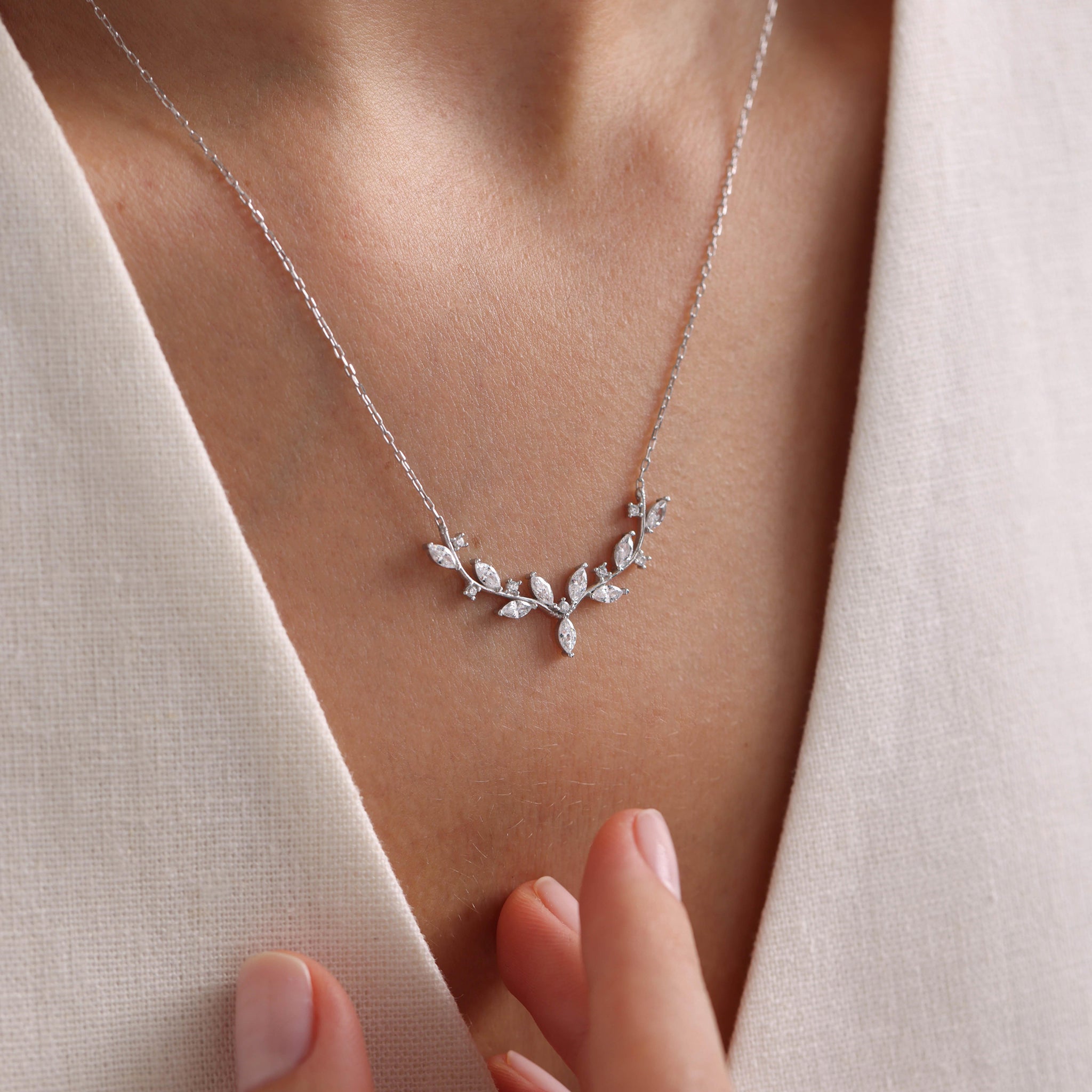 Silver necklace with leaf design on a person wearing a light-colored top.