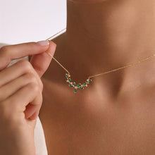 Gold necklace with green gemstones being worn on a person's neck.