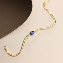 Gold bracelet with a blue gemstone on a beige background