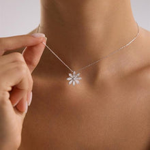 Silver necklace with a flower pendant being adjusted on a person's neck.