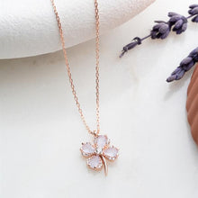 Rose gold necklace with a clover-shaped pendant on a white surface with lavender flowers.