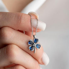 Silver necklace with a blue gemstone pendant held by a hand against a neutral background