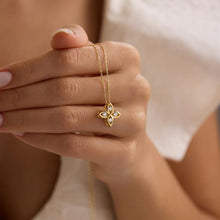 Gold necklace with a floral pendant held by a hand against a neutral background