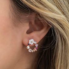 Close-up of an ear wearing a floral hoop earring with colorful gemstones.