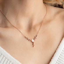 Rose gold necklace with a floral pendant on a person wearing a white top.