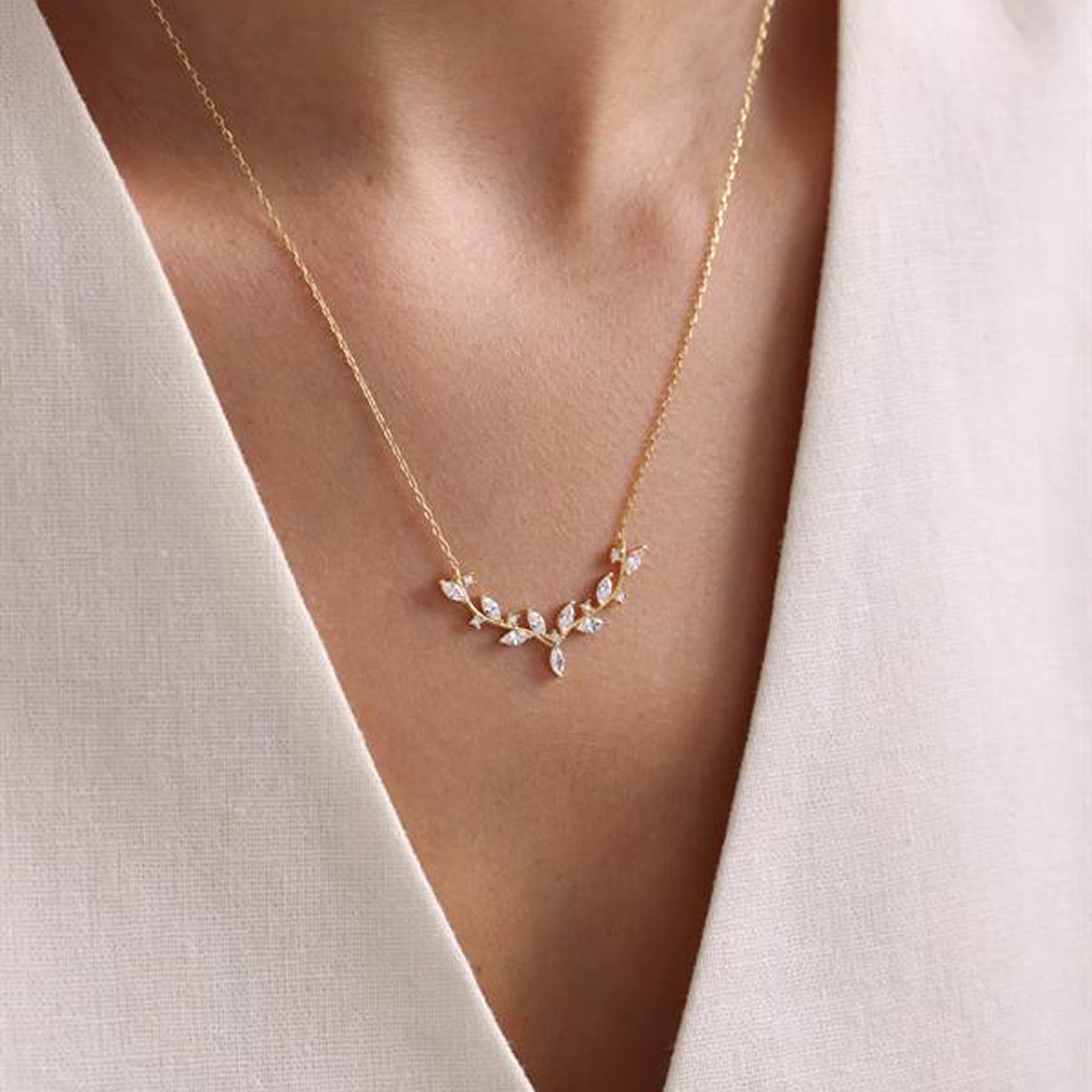 Delicate gold necklace with small stones worn by a person against a neutral background