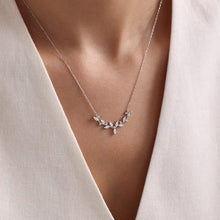 Necklace with a delicate leaf design worn by a person in a light-colored outfit.