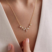 Gold necklace with diamond-like stones worn by a person against a neutral background