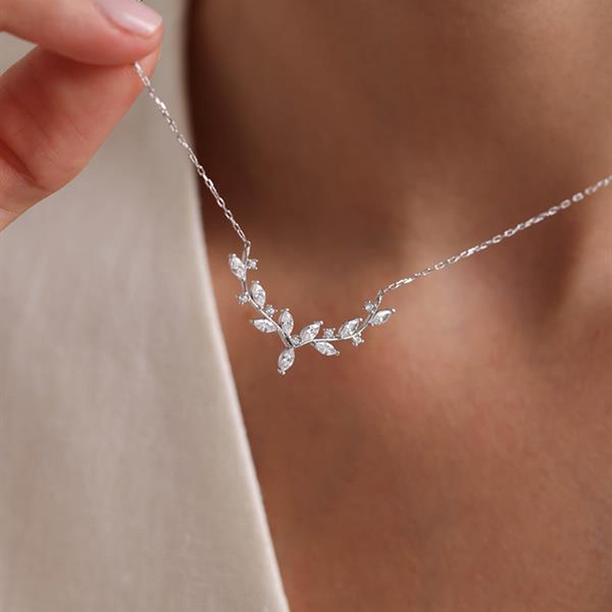 Silver leaf necklace being worn on a blurred background