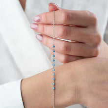 Hand wearing a delicate silver bracelet with blue beads on a plain background
