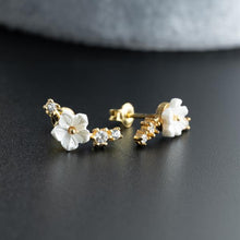 Pair of gold and white floral earrings on a dark surface