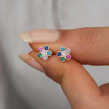Multicolored gemstone earrings held between fingers against a neutral background