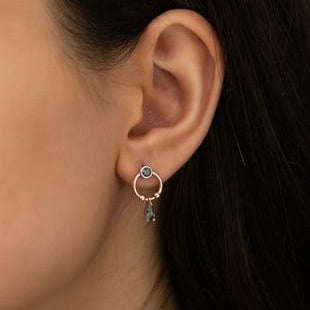 Close-up of an ear wearing a small hoop earring with a dark gemstone.