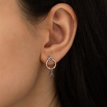 Close-up of an ear wearing a small hoop earring with a dark gemstone.