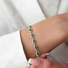 Silver bracelet with green gemstones on a wrist against a white background