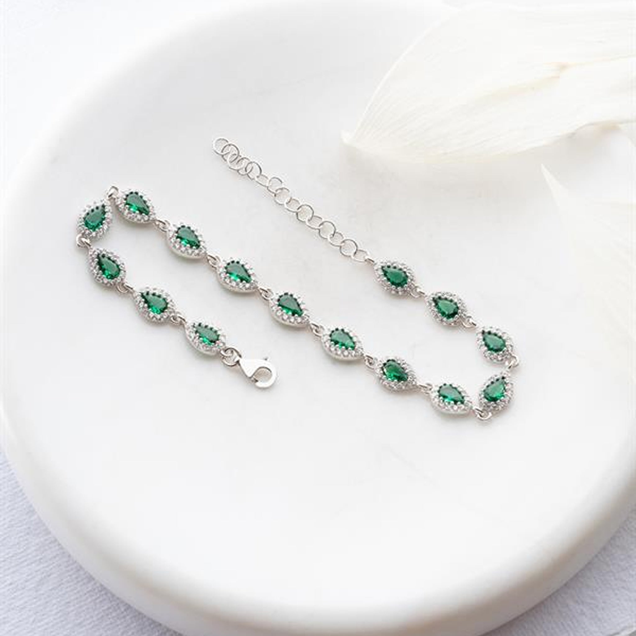 Silver bracelet with green gemstones on a white plate