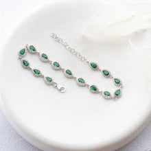 Silver bracelet with green gemstones on a white plate