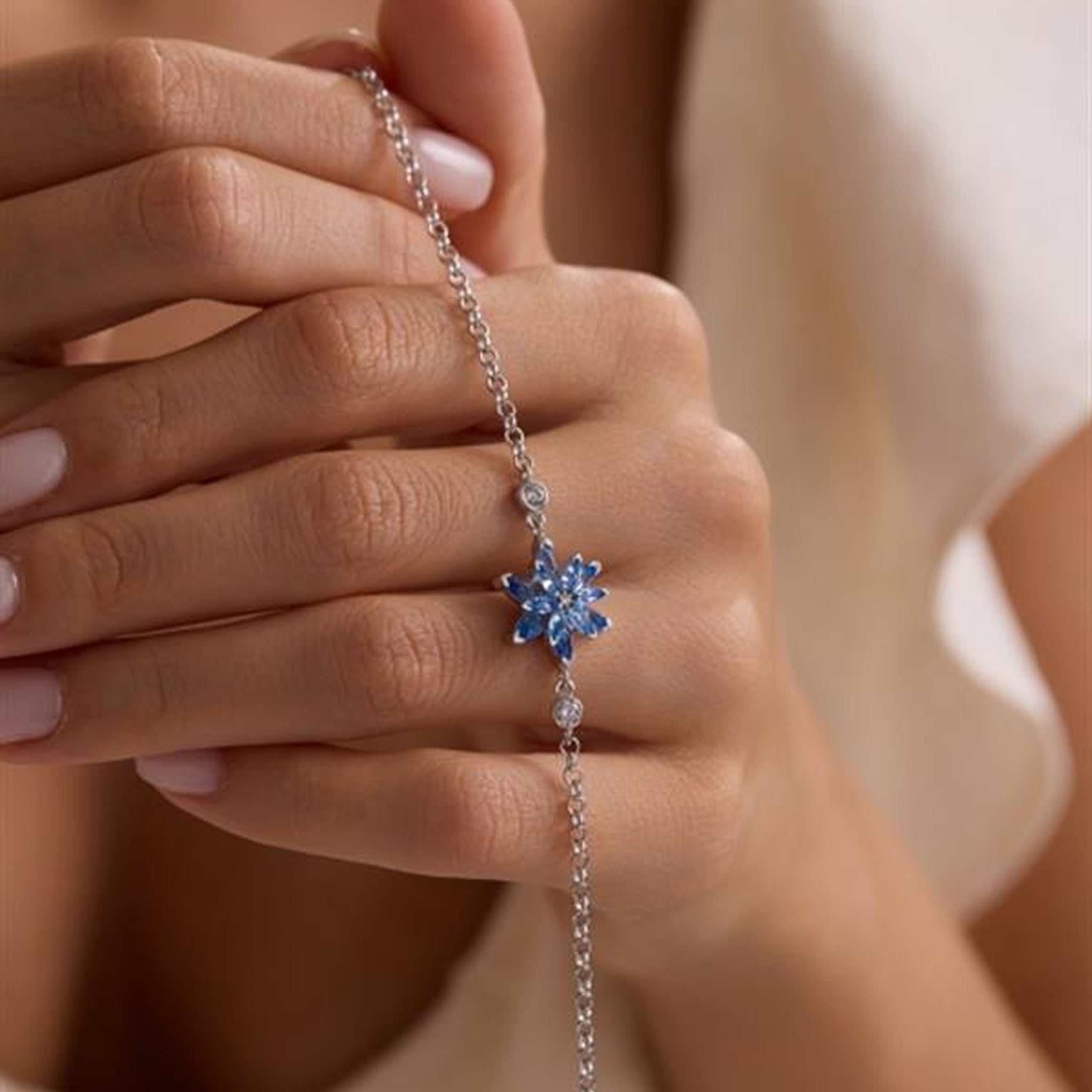Close-up of a hand wearing a silver bracelet with a blue gemstone on a neutral background