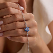 Close-up of a hand wearing a silver bracelet with a blue gemstone on a neutral background