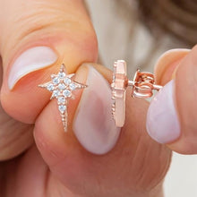 Rose gold star-shaped earrings held between fingers with a blurred background