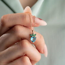 Hand holding a necklace with a heart-shaped blue gemstone pendant against a blurred background
