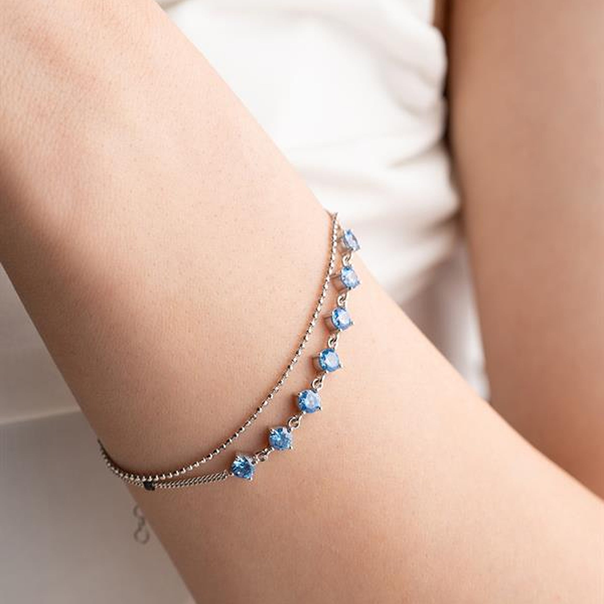 Close-up of a person's arm wearing a bracelet with blue gemstones on a blurred background