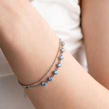 Close-up of a person's arm wearing a bracelet with blue gemstones on a blurred background