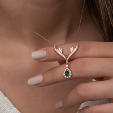 Rose gold necklace with a green gemstone pendant held by a hand against a neutral background