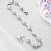 Silver bracelet on a light gray surface with a small dish of pearls in the background.