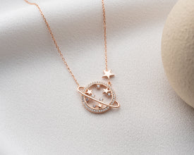 A glowing silver Saturn necklace photographed under soft lighting to emphasize its polished finish and planetary details.