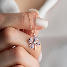 Hand holding a delicate necklace with a flower-shaped pendant against a blurred background