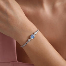 Silver bracelet with a blue gemstone on a wrist against a soft pink background