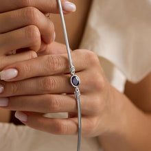 Close-up of a hand holding a silver bracelet with a purple gemstone.