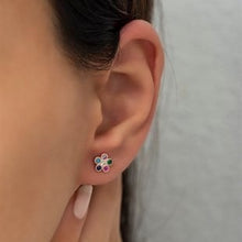 Close-up of an ear wearing a colorful flower-shaped earring against a neutral background