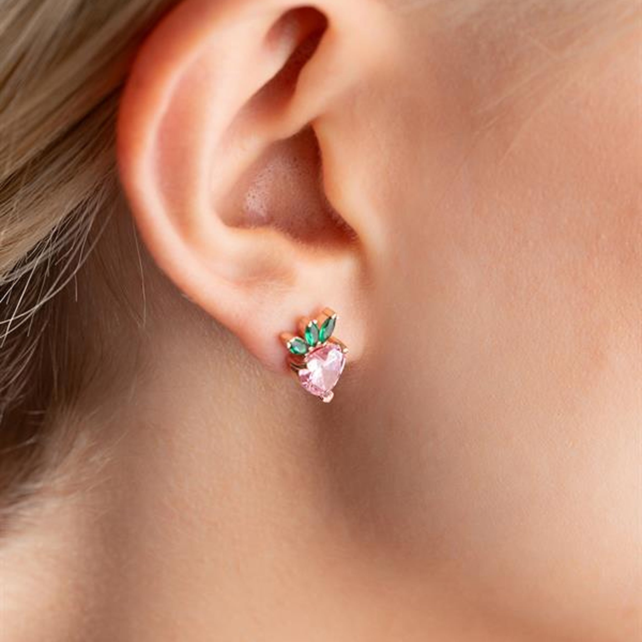 Close-up of an ear wearing a pink heart-shaped earring with green stones.