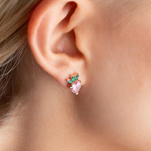 Close-up of an ear wearing a pink heart-shaped earring with green stones.