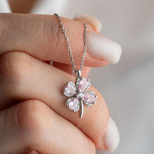 Pink clover-shaped pendant on a chain held by a hand with light nail polish.