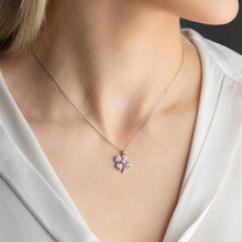 Necklace with a pink flower pendant worn by a person in a white top.