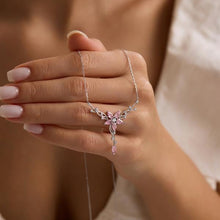 Hand holding a delicate necklace with a pink flower pendant against a blurred background