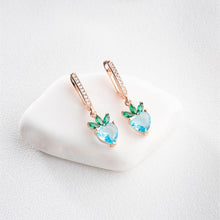 Pair of earrings with green and blue gemstones on a white heart-shaped stand.
