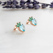 Rose gold earrings with green and blue gemstones on a light background