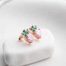 Pair of earrings with pink and green gemstones on a white stone surface